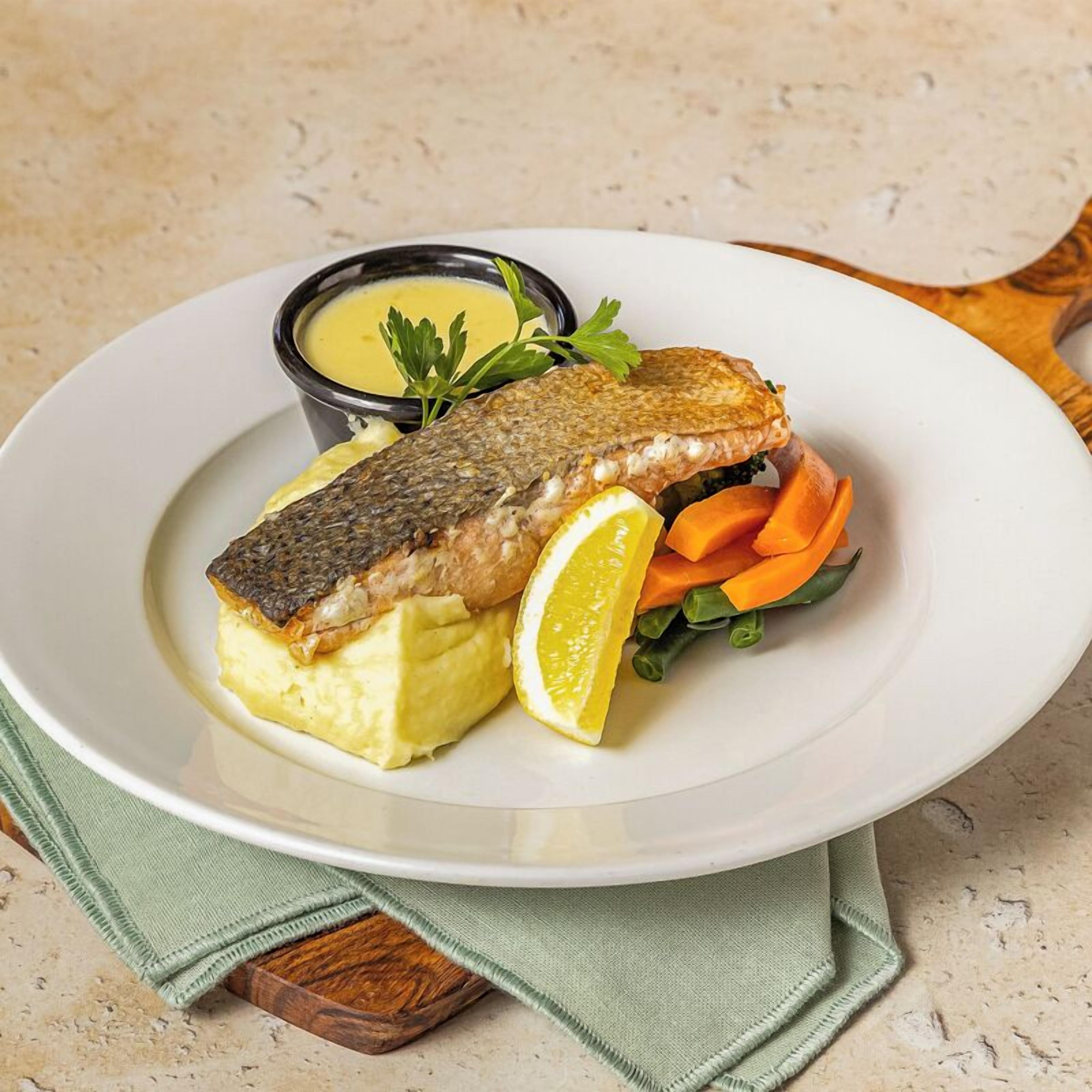 A plate with a fish fillet, mashed potatoes, carrots, and a lemon wedge, accompanied by a small bowl of sauce.