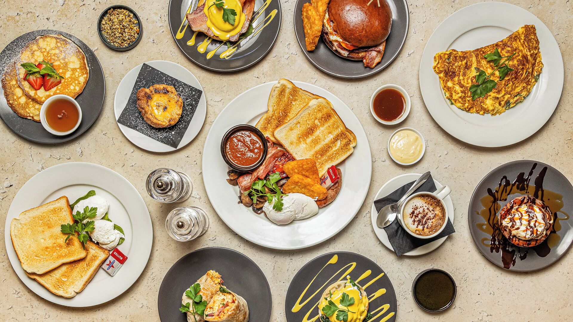 Une variété de plats pour le petit-déjeuner sont présentés sur des assiettes, notamment des crêpes, des omelettes et des toasts.