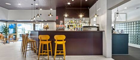 A bar area with wooden stools, a counter with a variety of bottles, and pendant lighting.