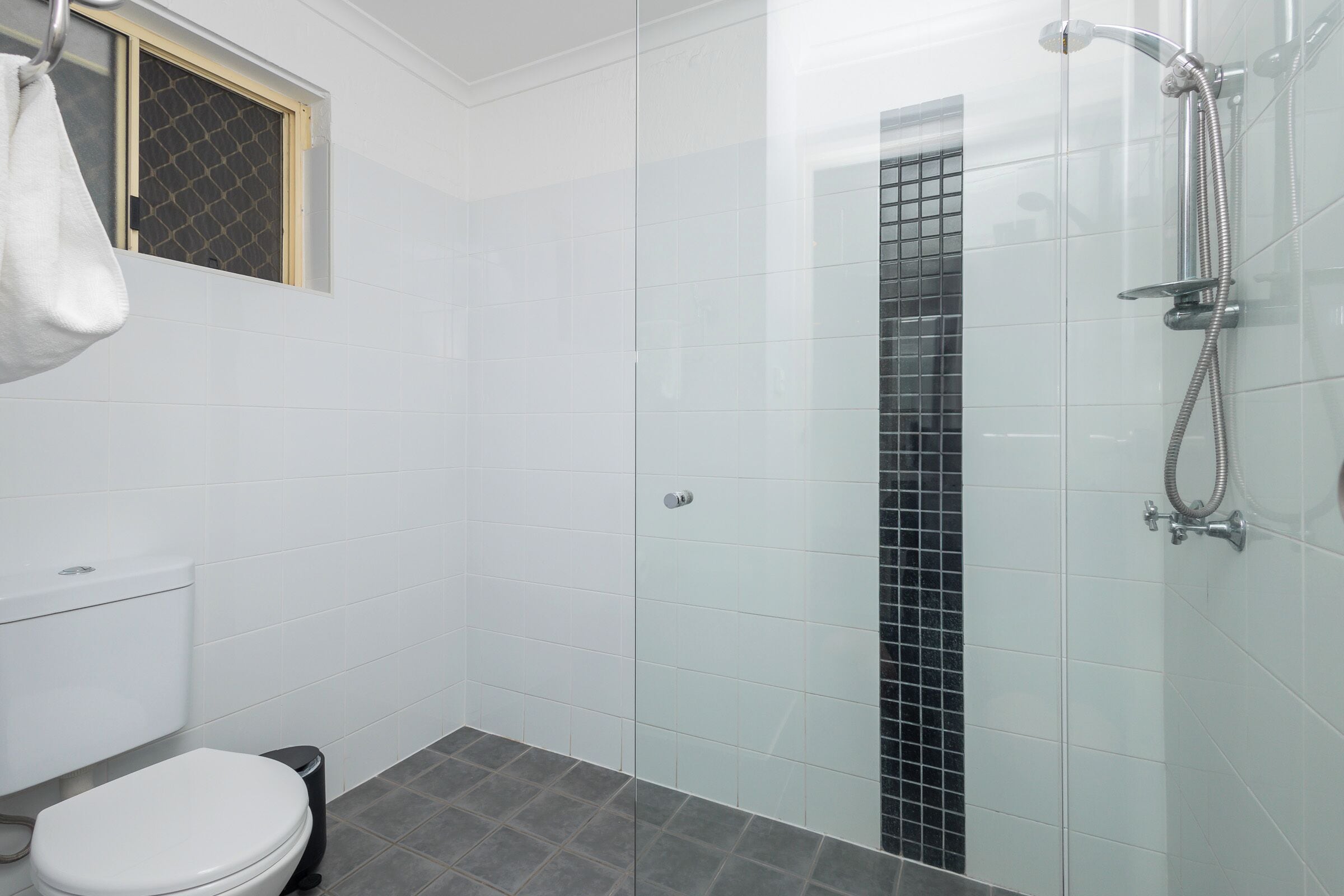 Ein Badezimmer mit Toilette, Dusche und einem Fenster mit Insektenschutzgitter.