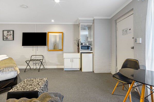 Habitación de hotel compacta con cama, kitchenette pequeña, televisión, espejo y zona de comedor.
