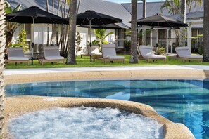 A pool area with lounge chairs and umbrellas, surrounded by palm trees and a building with a modern design. - Ballina Byron Islander Resort and Conference Centre (West Ballina)