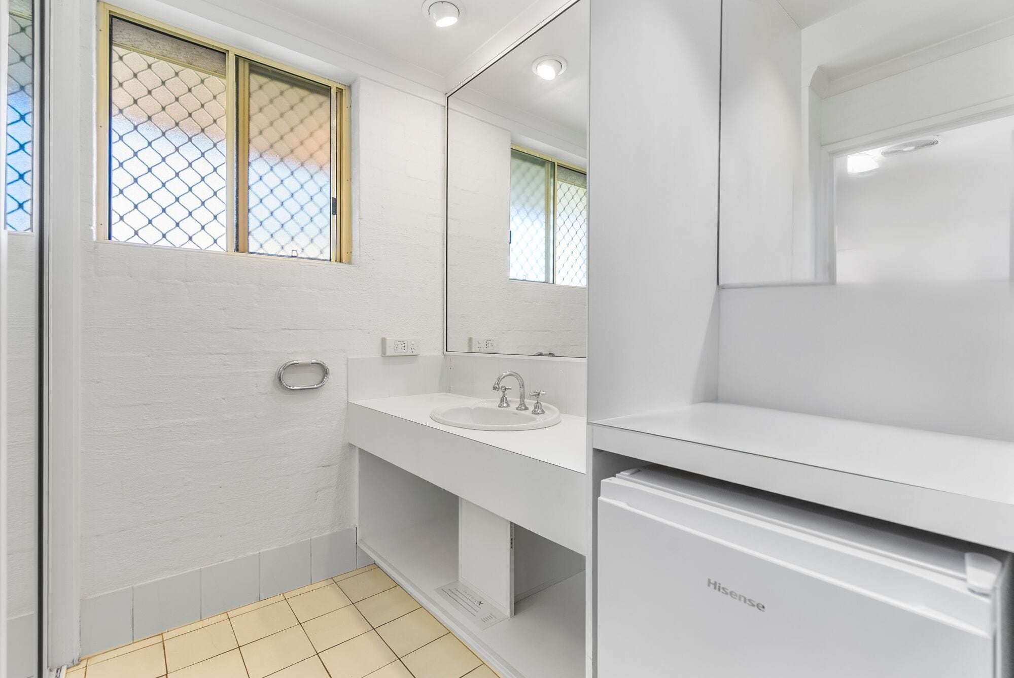 A modern bathroom with a white sink, mirror, and a Hisense refrigerator.