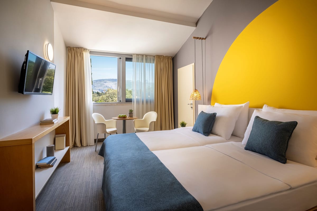 A hotel room with a bed, a desk, a TV, a window with curtains, and a view of the outdoors.