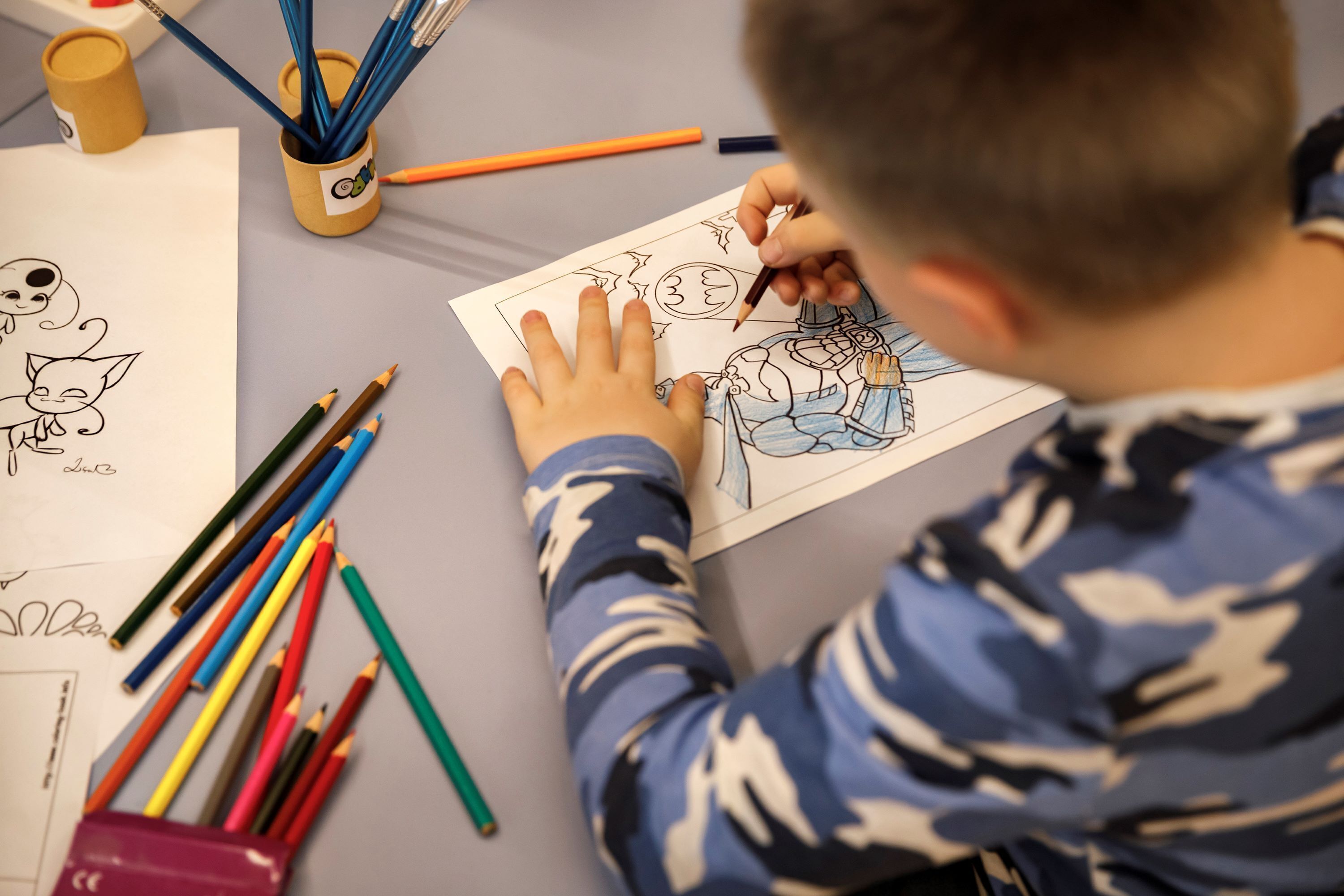 Un niño dibujando con lápices de colores sobre una mesa.