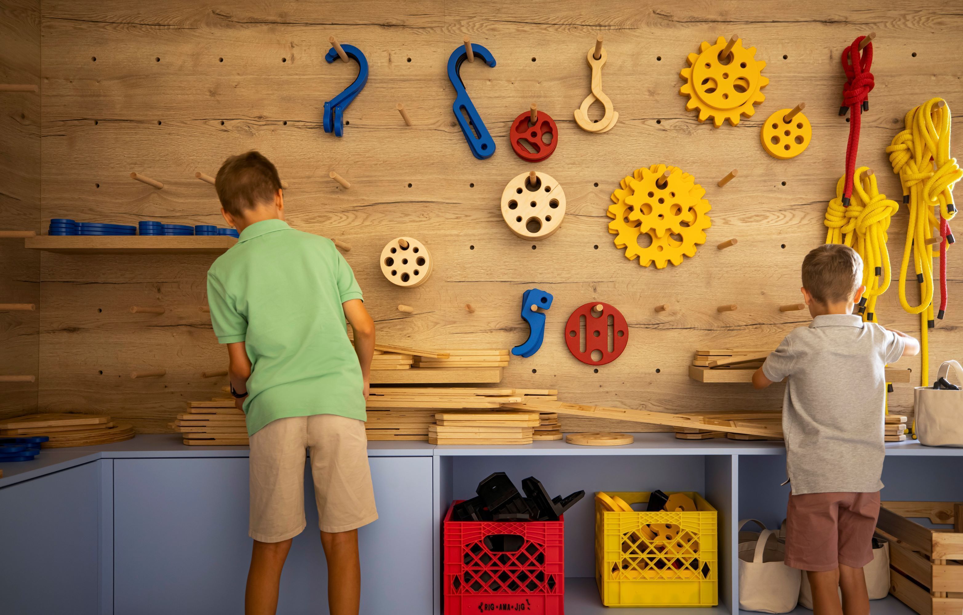 Two children playing with wooden shapes and tools on a shelf.
