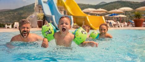 A swimming pool with water slides and umbrellas in the background.
