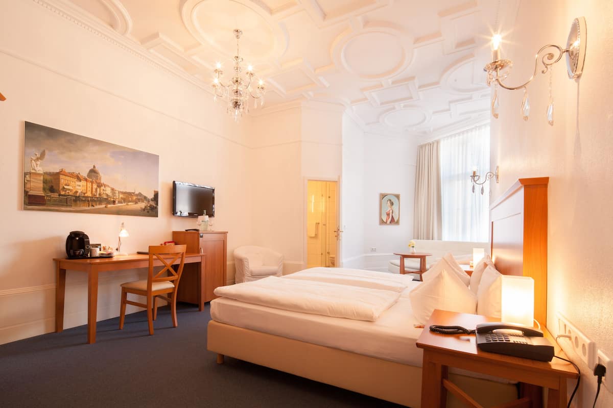 Habitación de hotel con cama, escritorio, silla y un cuadro de un paisaje urbano.