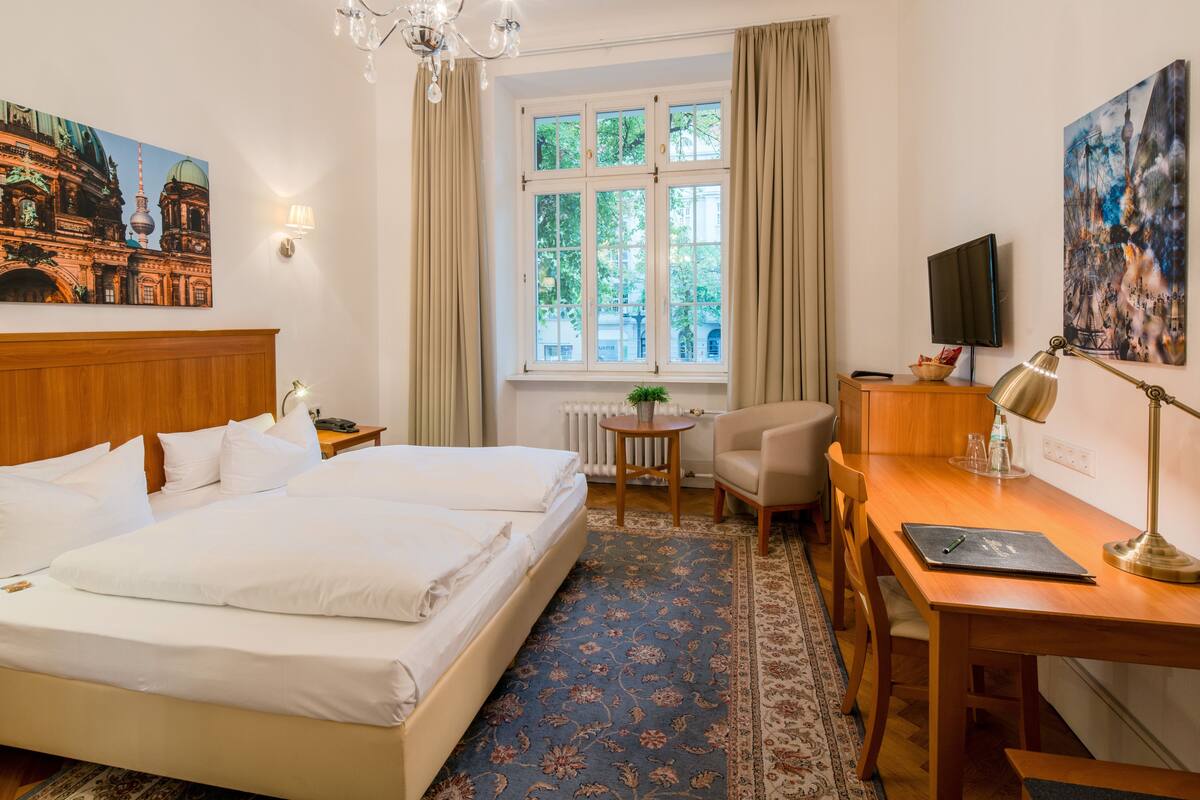 Habitación de hotel con cama doble, escritorio con silla, televisor y ventana con cortinas.