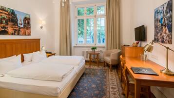 A hotel room with a double bed, a desk with a chair, a television, and a window with curtains.