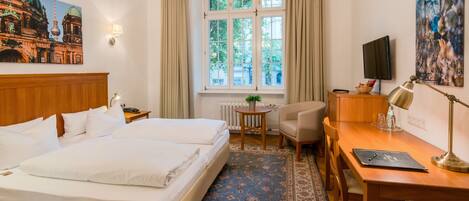 A hotel room with a double bed, a desk with a chair, a television, and a window with curtains.