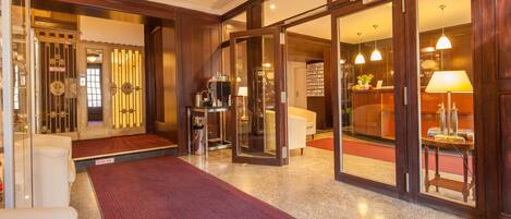 A hotel lobby with a red carpet, wooden doors, and a reception desk.
