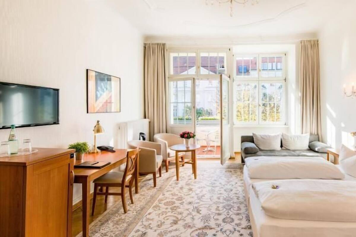 Habitación de hotel con cama, escritorio con silla, televisión y ventana con cortinas.