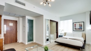 A modern hotel room with a bed, a glass coffee table, a sofa, and a bathroom visible through an open door. - Congress Suites at the Strand (Miami Beach)