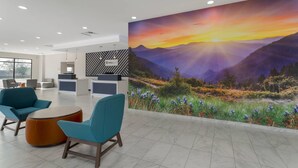 Eine moderne Lobby mit Türkis-Stühlen, einem runden Tisch und einer großen Wandmalerei mit Sonnenuntergang über Bergen.