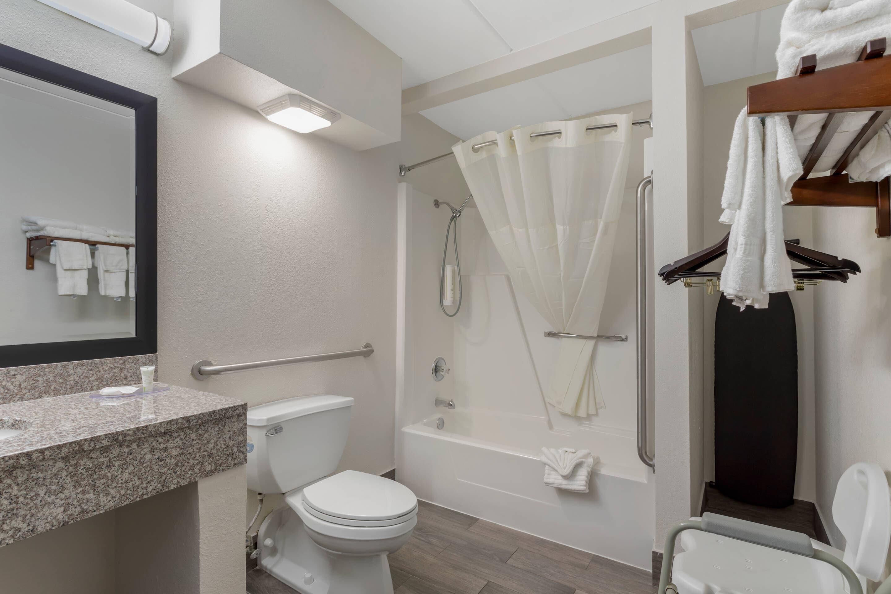A modern bathroom with a toilet, sink, shower, and a wheelchair-accessible bench.