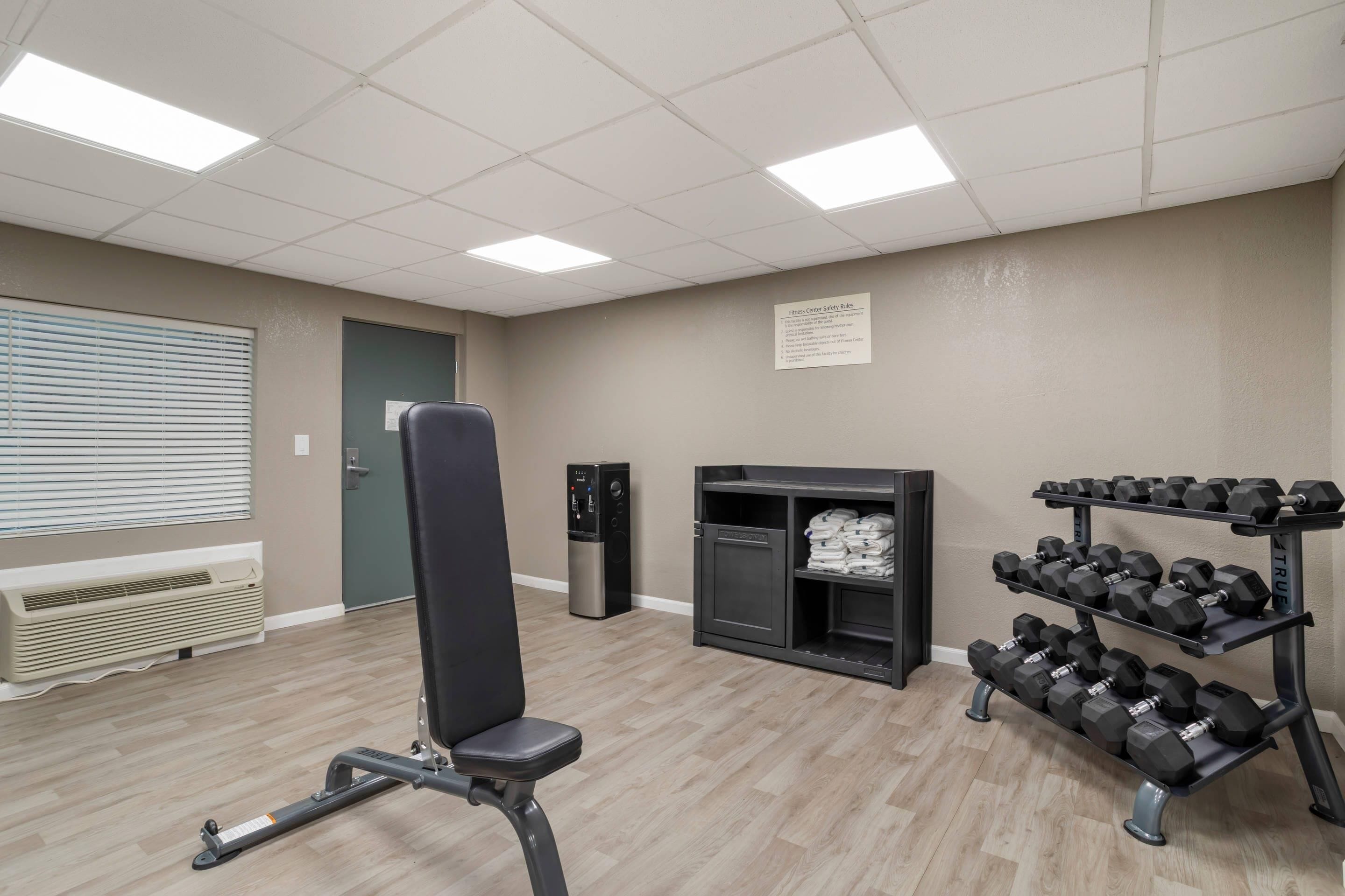 Une salle de sport équipée de matériel d’exercice, d’un distributeur d’eau et d’un panneau fixé au mur.