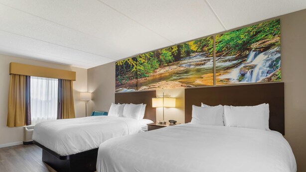 Ein Hotelzimmer mit zwei Betten, einem großen Gemälde eines Wasserfalls, einem Fenster mit Vorhängen und einem Nachttisch mit Lampe.