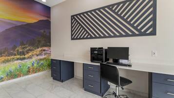 A modern office space with a desktop computer, a chair, and a decorative wall with a nature scene and geometric patterns.