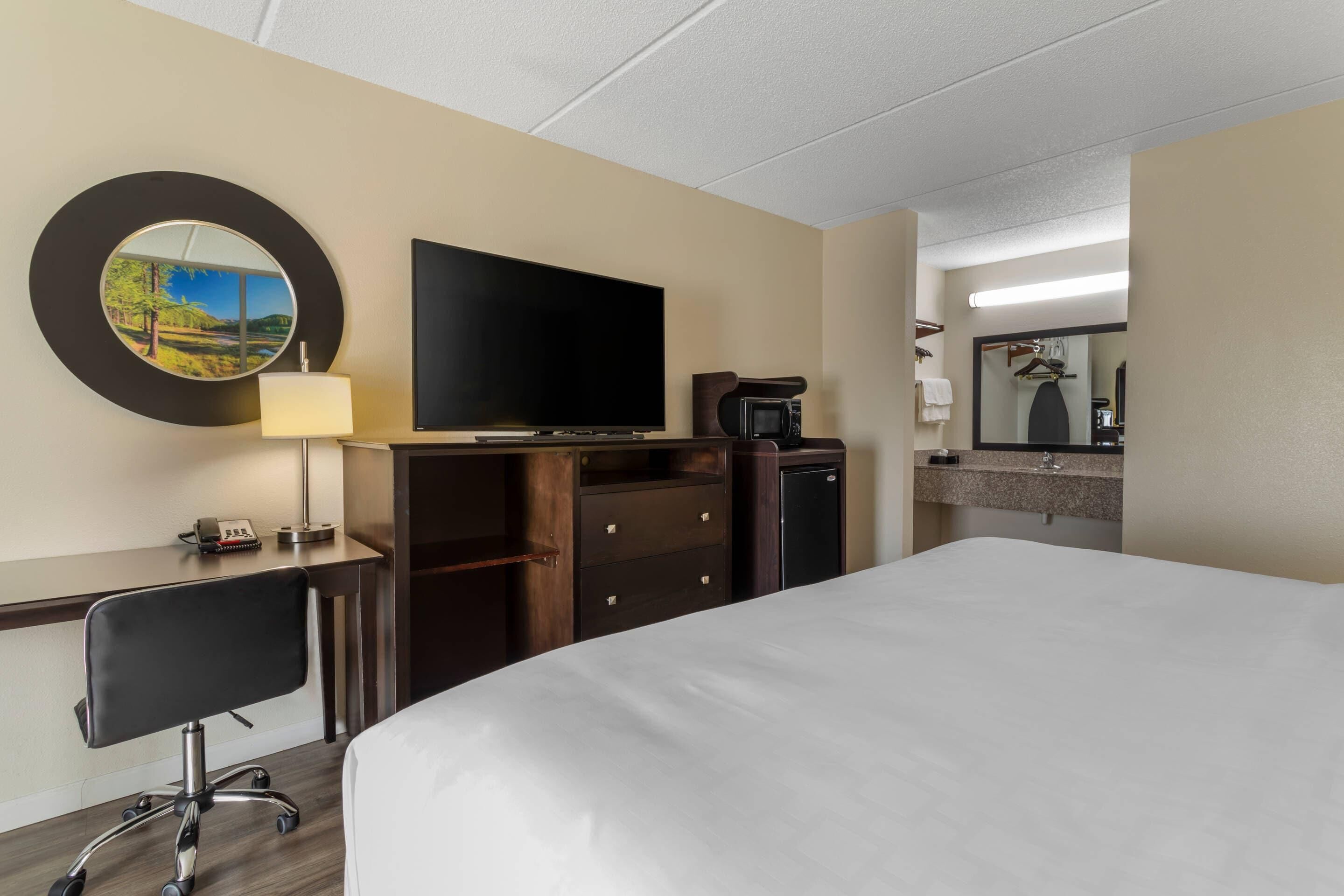 Una habitación de hotel con una cama grande, un escritorio con silla, televisor de pantalla plana, microondas, cafetera y espejo.