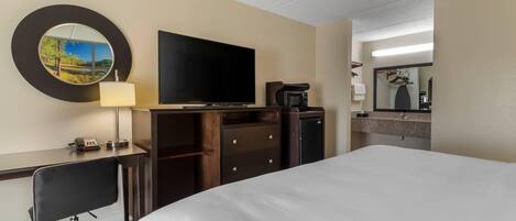 Una habitación de hotel con una cama grande, un escritorio con silla, televisor de pantalla plana, microondas, cafetera y espejo.