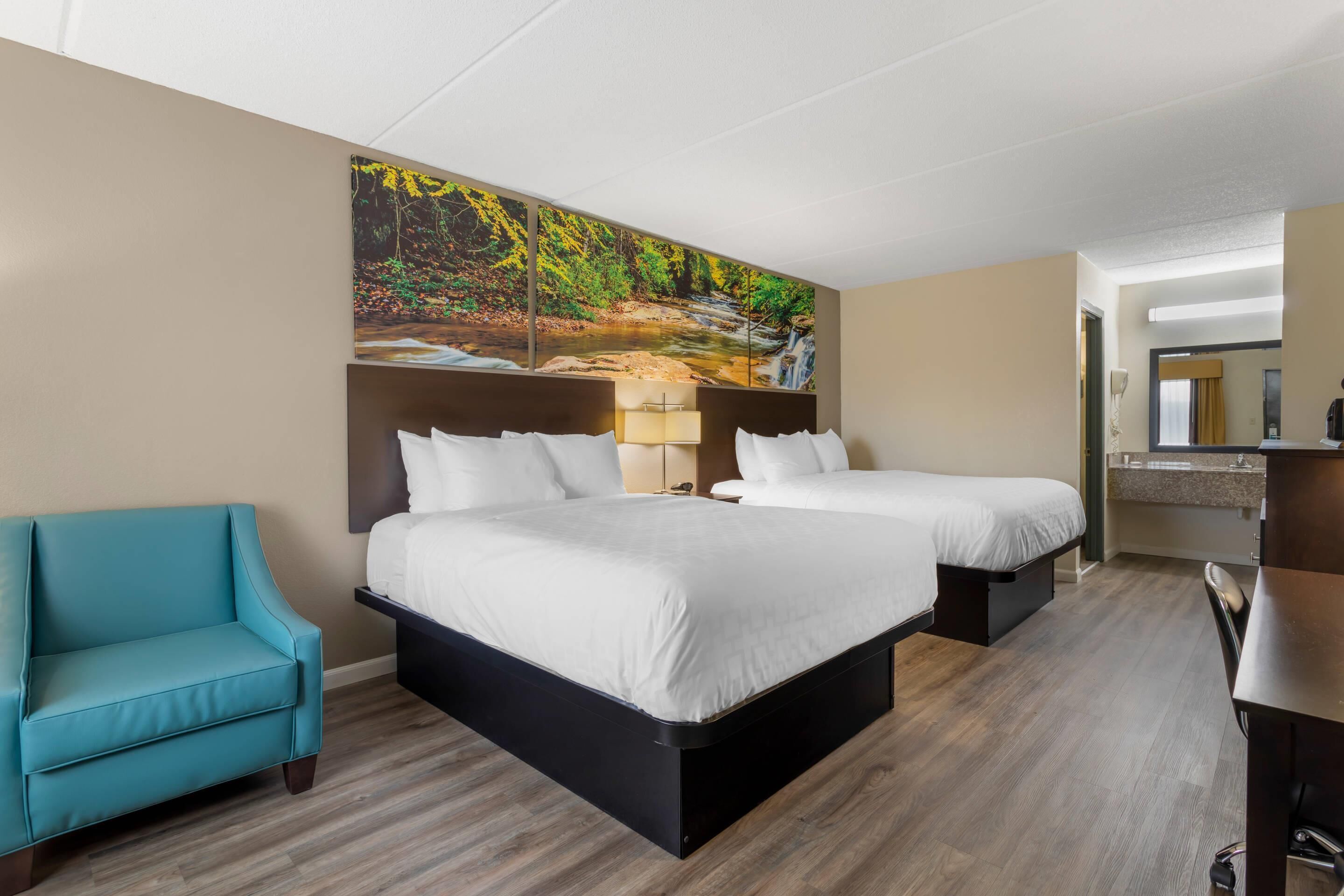 A hotel room with two beds, a sofa, a desk, and a large painting of a forest stream on the wall.