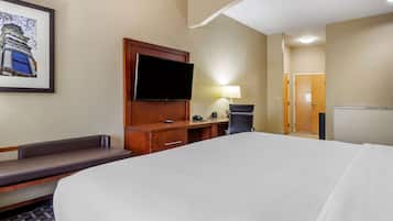A hotel room with a large bed, a flat-screen TV mounted on the wall, a desk with a lamp, and a bench.