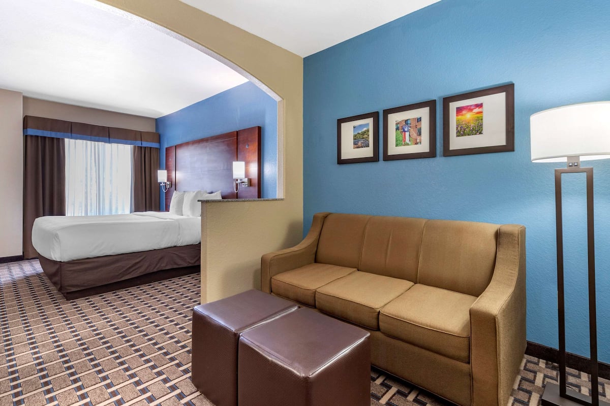 A hotel room with a bed, a sofa, a small table, and a lamp. There are three framed pictures on the wall.