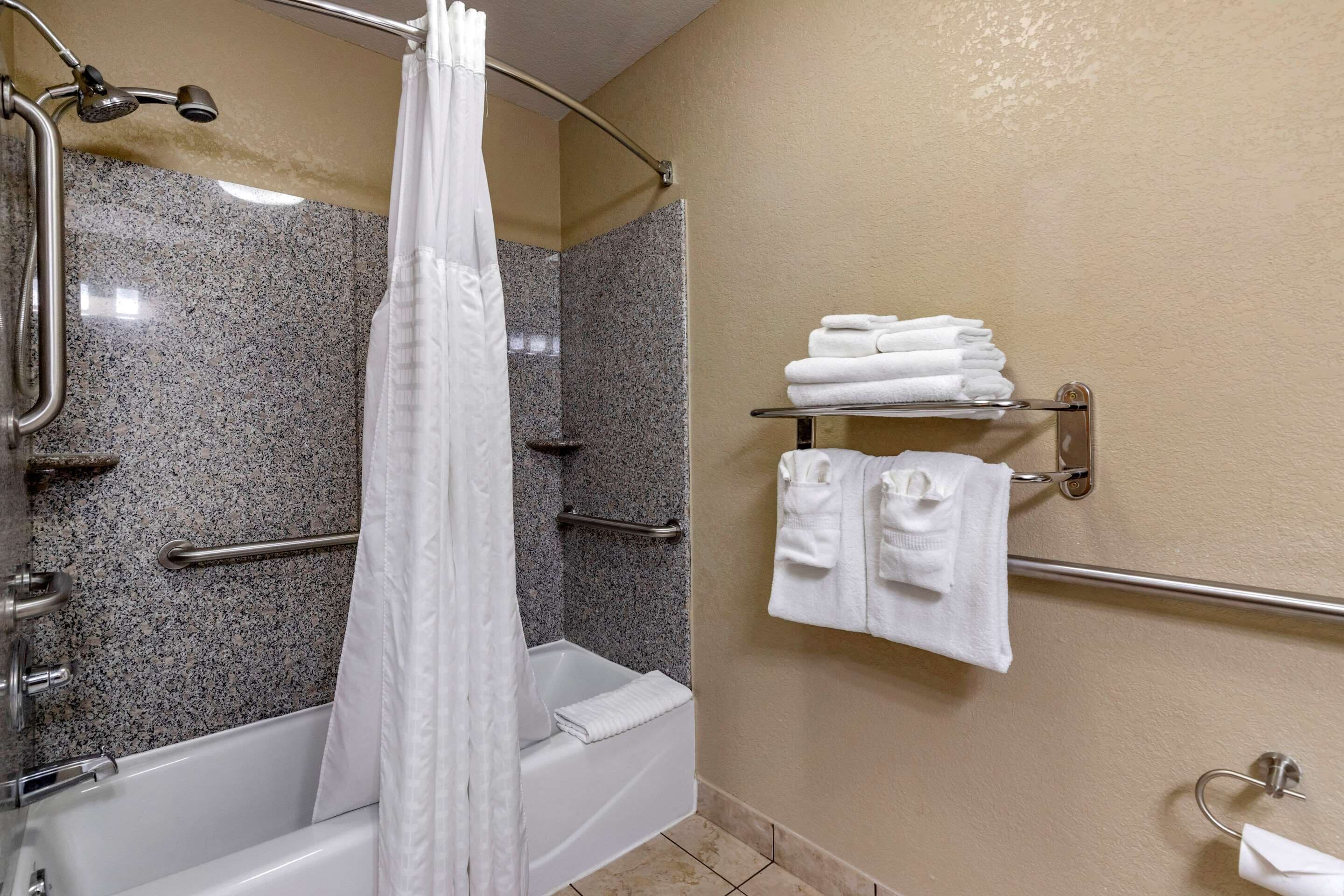 A bathroom with a shower, grab bars, a bathtub, and a towel rack with folded towels.