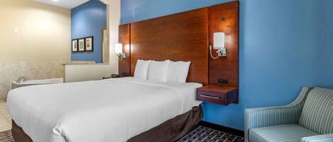 A hotel room with a large bed, a nightstand, a chair, and a bathroom with a bathtub.