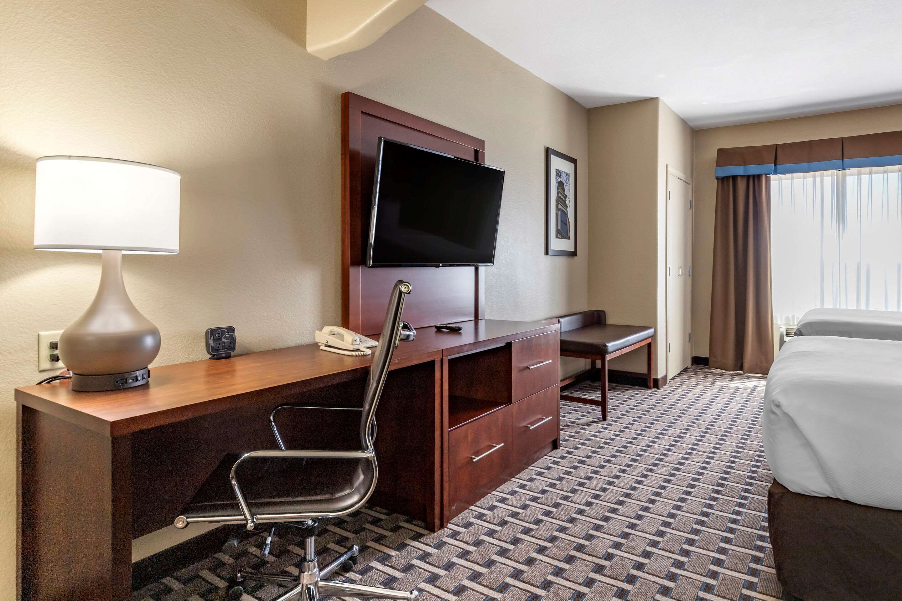 Une chambre d’hôtel avec un bureau en bois, une chaise, une télévision, un lit et une moquette à motifs.
