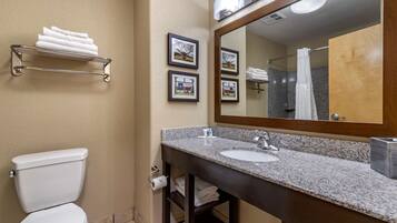 A bathroom with a toilet, sink, and mirror. There are towels on a shelf and framed pictures on the wall.