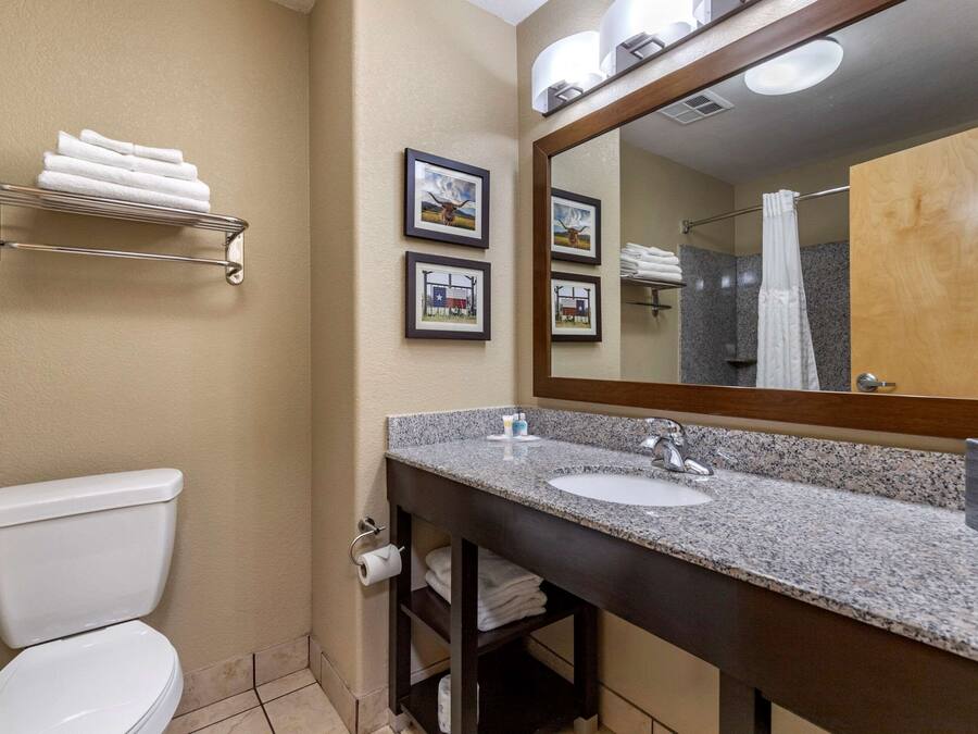 A bathroom with a toilet, sink, and mirror. There are towels on a shelf and framed pictures on the wall.
