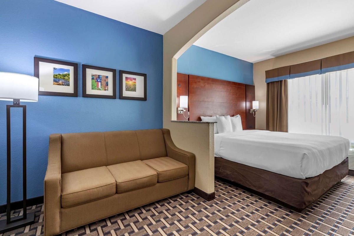 A hotel room with a bed, a sofa, a desk, and a window with curtains.