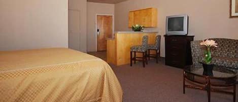 A hotel room with a bed, a desk with a chair, a television, and a small table with a vase.