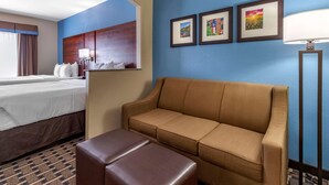 A hotel room with a bed, a sofa, a small table, and a lamp. There are three framed pictures on the wall.