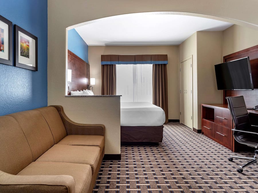 A hotel room with a sofa, a bed, a desk with a chair, a television, and a wardrobe.