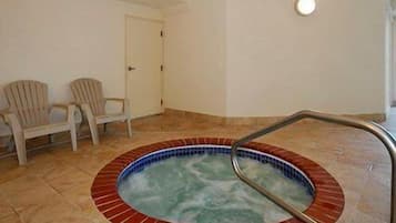 Un pequeño jacuzzi interior con borde de azulejos y una escalera de metal. Hay dos sillas contra la pared.