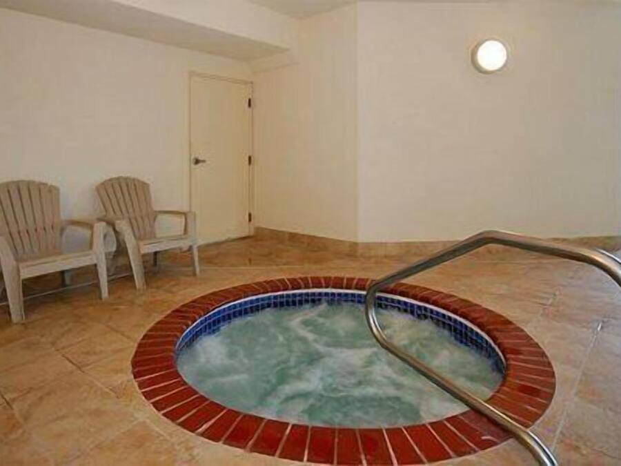 Un pequeño jacuzzi interior con borde de azulejos y una escalera de metal. Hay dos sillas contra la pared.