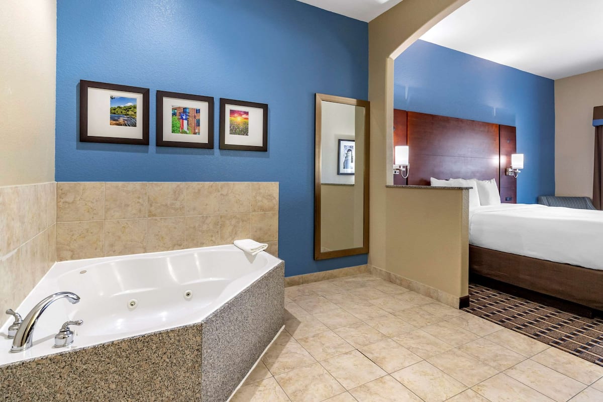 A hotel bathroom with a large bathtub, a bed, and three framed pictures on the wall.