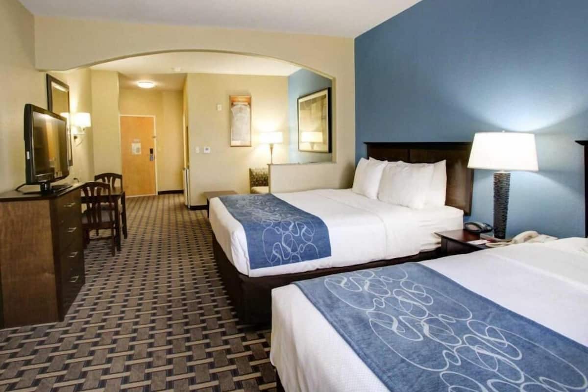 A hotel room with two beds, a desk with a TV, a chair, and a hallway leading to another room.