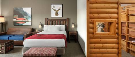A hotel room with a bed, a wooden bench, a suitcase, a lamp, and a wooden wall structure.