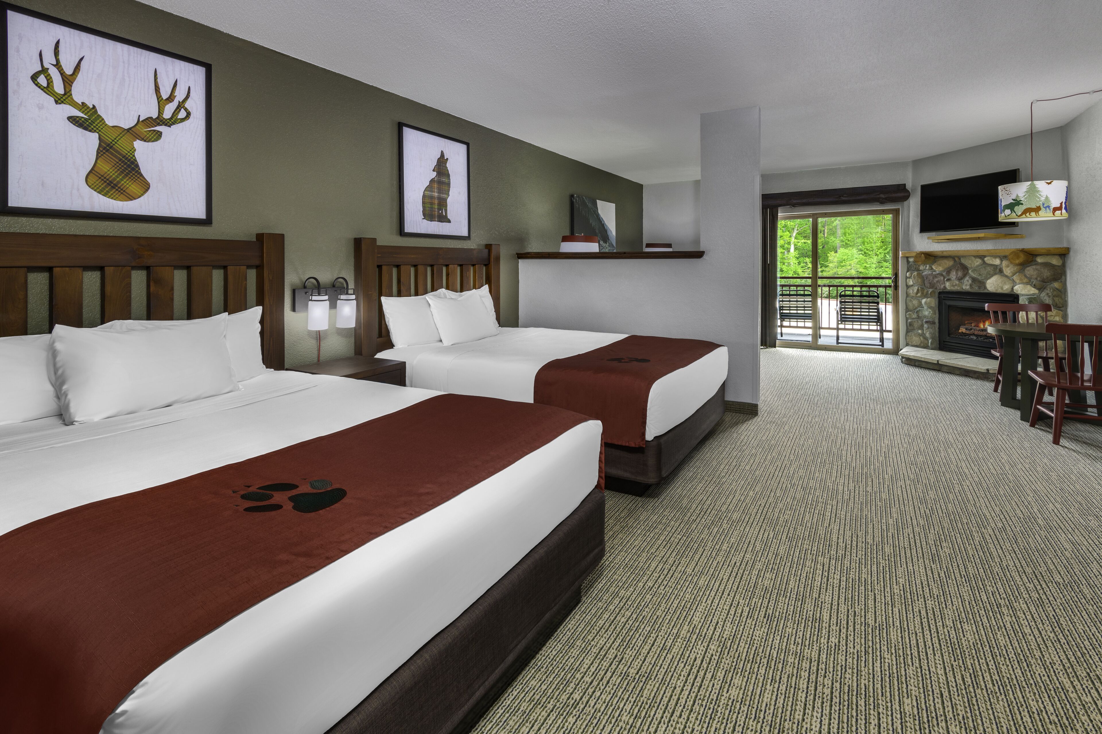 A hotel room with two beds, a fireplace, a TV, and a balcony with outdoor seating.