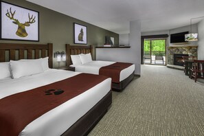 Habitación de hotel con dos camas, chimenea, televisor y balcón con mobiliario exterior.