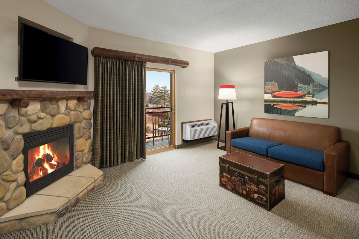 A living room with a stone fireplace, a flat-screen TV, a sofa, a lamp, and a painting.