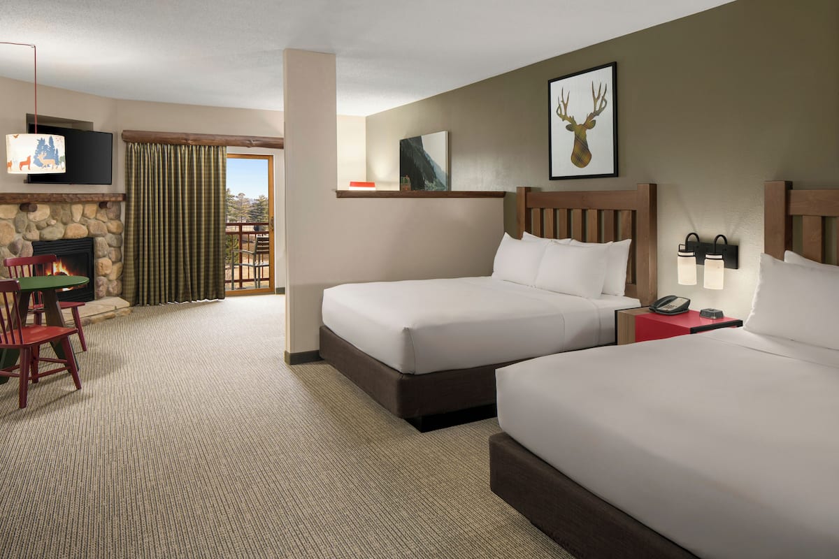 A hotel room with two beds, a TV, a fireplace, a dining area, and a balcony.