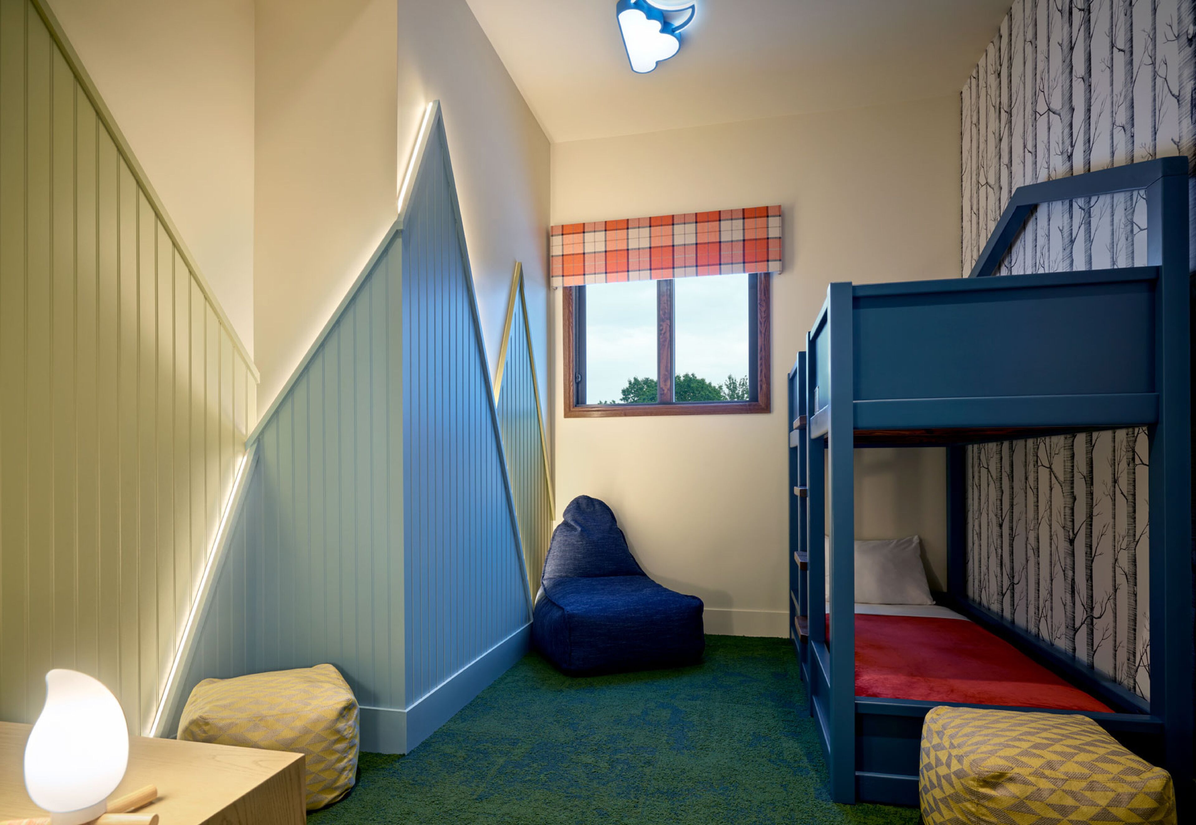 Une chambre d’enfant avec des lits superposés, un fauteuil poire, un bureau avec une lampe et une fenêtre donnant sur un beau paysage.