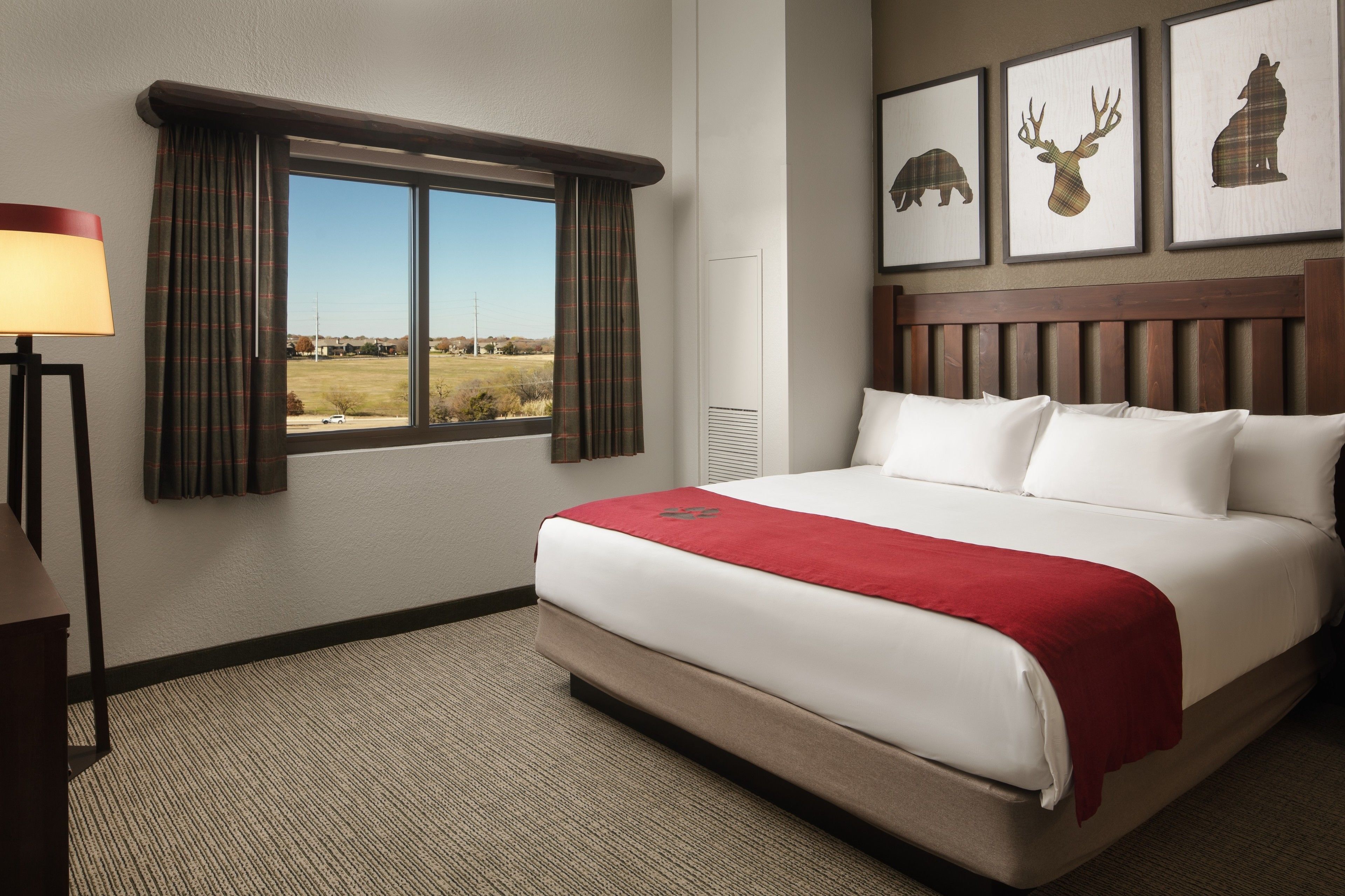 Una habitación de hotel con una cama grande, una ventana con cortinas, una lámpara y tres cuadros en la pared.