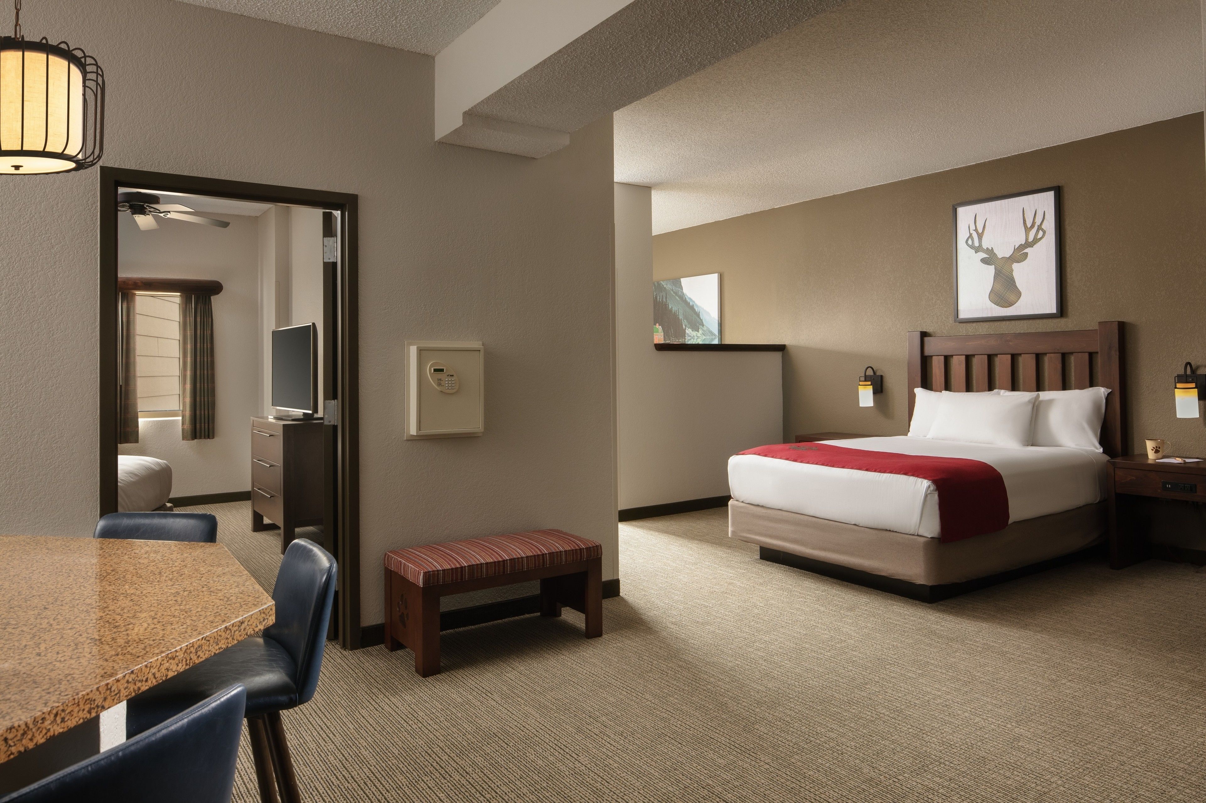 A hotel room with a bed, a desk, a chair, a bench, a bedside table, and a wall-mounted artwork.