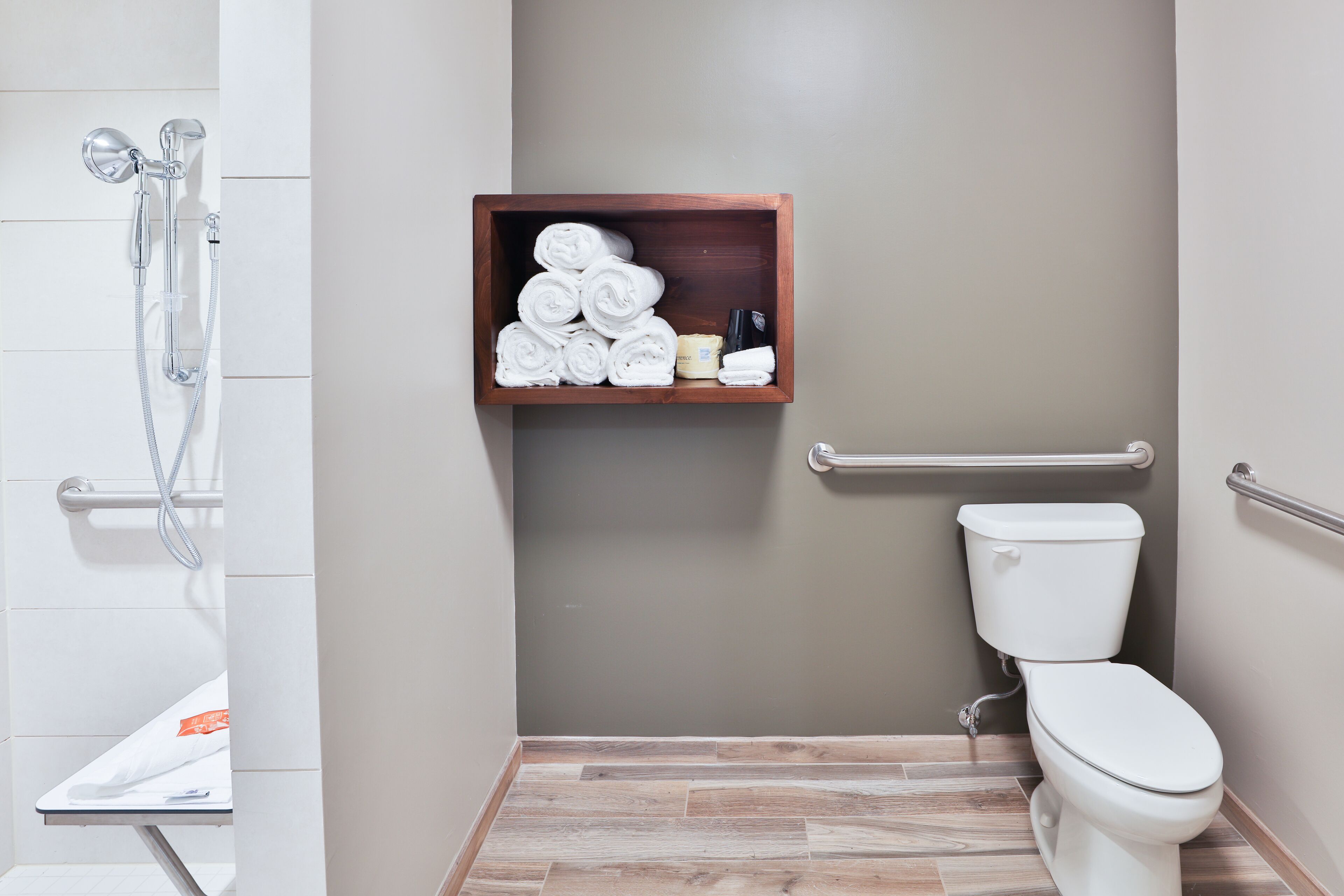 Un baño con ducha, inodoro y un estante de madera con toallas y artículos de aseo.